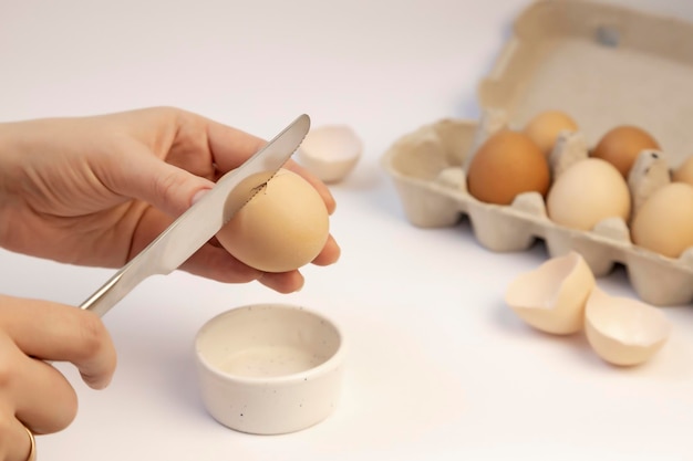 Une main féminine tient un œuf de poule et le casse avec un couteau Plateau en carton avec des œufs Focus sur l'œuf