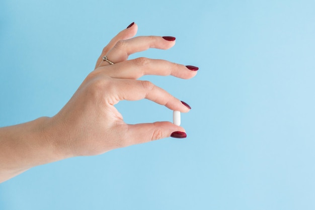 La main féminine tient une pilule blanche dans les doigts sur fond bleu Médicament antibiotique ou analgésique Femme prenant des médicaments