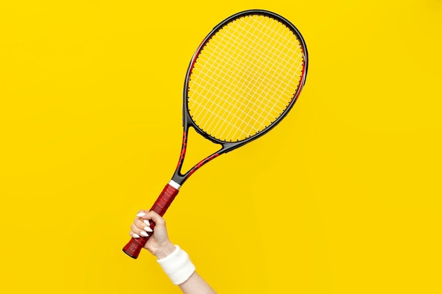 main féminine tient une raquette de tennis sur un fond jaune isolé équipement sportif gros plan