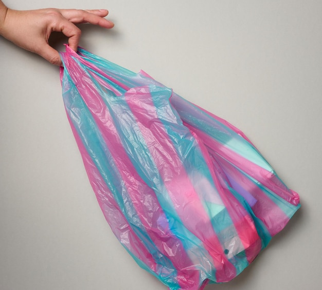 main féminine tient un sac en plastique plein sur fond gris vue supérieure