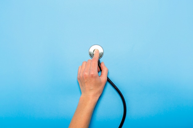 Main féminine tient un stéthoscope sur un bleu. Concept médecin, rendez-vous chez le médecin, virus, traitement, diagnostic. Mise à plat, vue de dessus