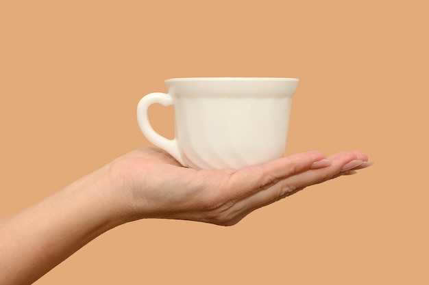 Une main féminine tient une tasse blanche. Minimalisme. Fermer. Sur fond beige. Concept.