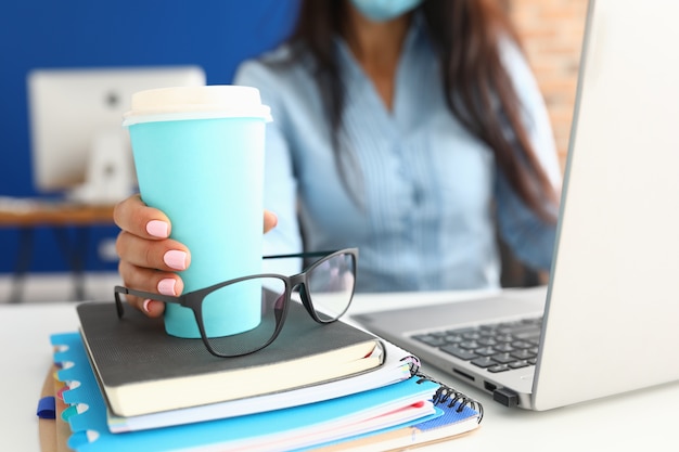 Main féminine tient une tasse de café sur le lieu de travail.