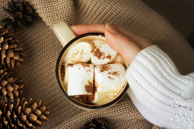 Une main féminine tient une tasse de chocolat chaud avec des guimauves composition d'hiver de vacances de noël