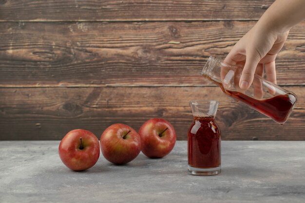 Main féminine verser du jus rouge dans le verre sur une surface en marbre.