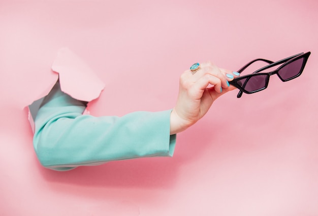 Main féminine en veste bleue classique avec des lunettes de soleil