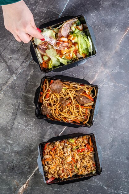 Main féminine avec vue de dessus de nourriture boeuf avec salade de nouilles udon et riz à la sauce tiriyaki Nourriture coréenne livrée dans des boîtes de récipient boîte de récipient de nourriture