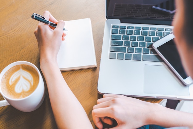 Main de femme d'affaires écrit sur un bloc-notes avec un stylo.