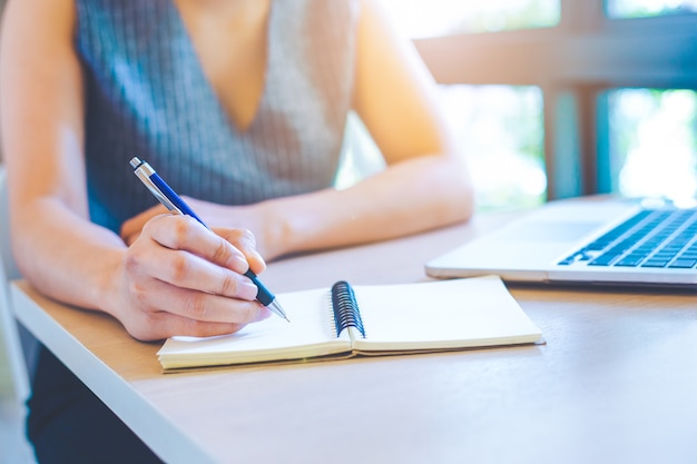 Main de femme d&#39;affaires écrit sur le bloc-notes