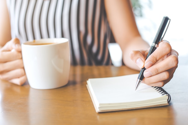 Main de femme d&#39;affaires écrit sur un carnet avec un stylo.