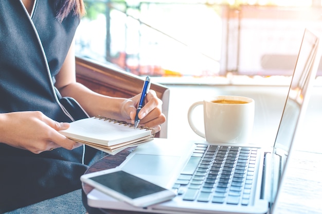 Main de femme d&#39;affaires travaille sur un ordinateur et écrit dans le bloc-notes.