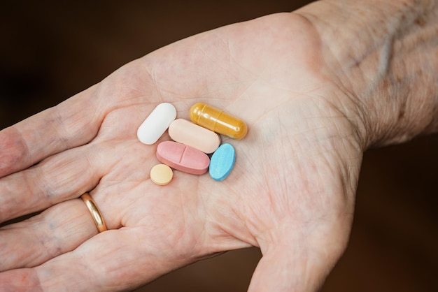 Main de femme âgée âgée tenant cinq pilules ou médicaments différents
