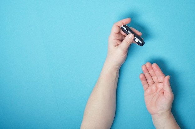 Main de femme à l'aide d'une lancette sur son doigt pour vérifier la glycémie à l'aide d'un glucomètre, diabète, glycémie, concept de soins de santé. vue de dessus de l'espace de copie de fond bleu