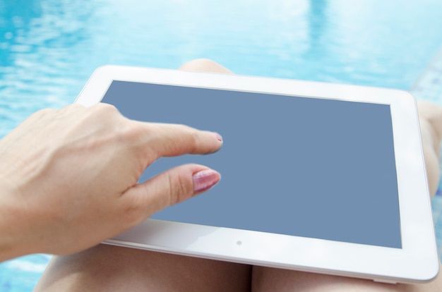 Main de femme à l&#39;aide de tablette numérique sur le côté de la piscine.