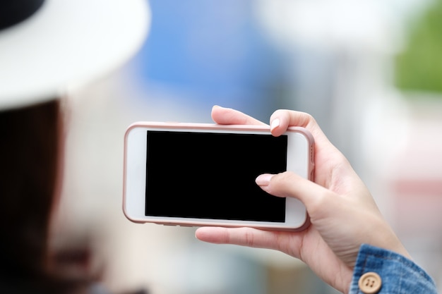 Main de femme à l&#39;aide de téléphone intelligent avec un écran blanc sur fond flou