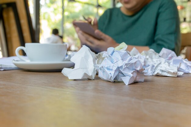 Main de femme à l&#39;aide de téléphone portable travaillant après les heures normales avec du papier froissé sur la table.