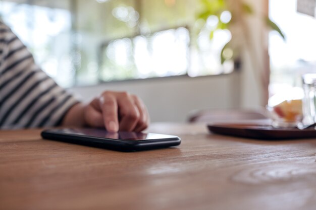 Une main de femme à l'aide et en touchant un écran de téléphone intelligent sur une table en bois