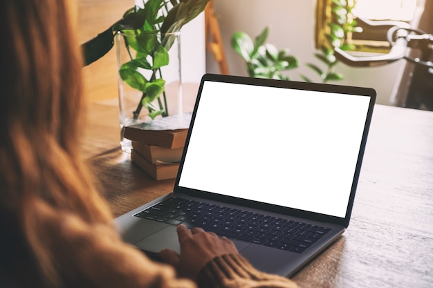 La main d'une femme à l'aide et en touchant le pavé tactile d'ordinateur portable avec écran de bureau blanc vierge sur table en bois