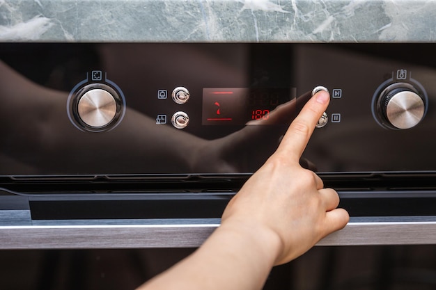 Main de femme allumant le four pour faire un gâteau à la maison gros plan du bouton du four vue de l'el noir