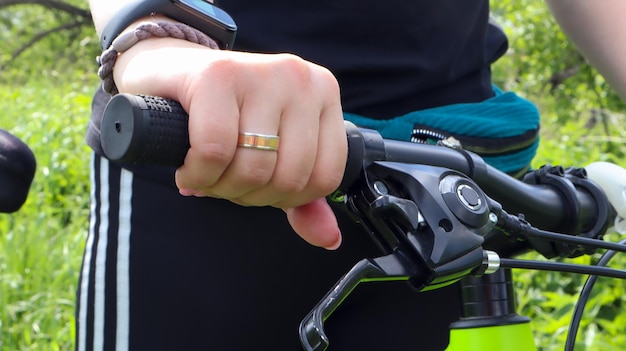 Main de femme avec anneau sur le guidon d'un vélo de montagne dans le parc en gros plan. Le motard s'appuie sur le guidon du vélo.