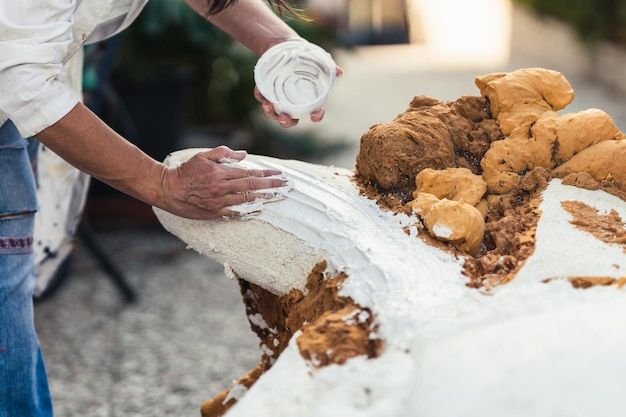 Main d'une femme appliquant de la pâte sur la surface d'une figure en polystyrène