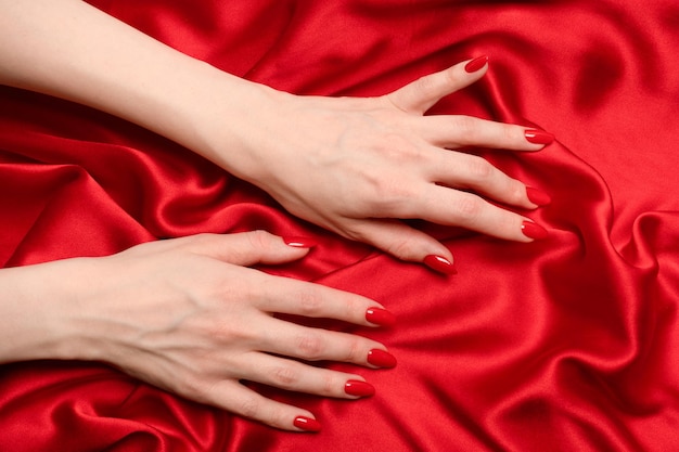 La main d'une femme aux ongles rouges essaie d'arracher un tissu de soie rouge