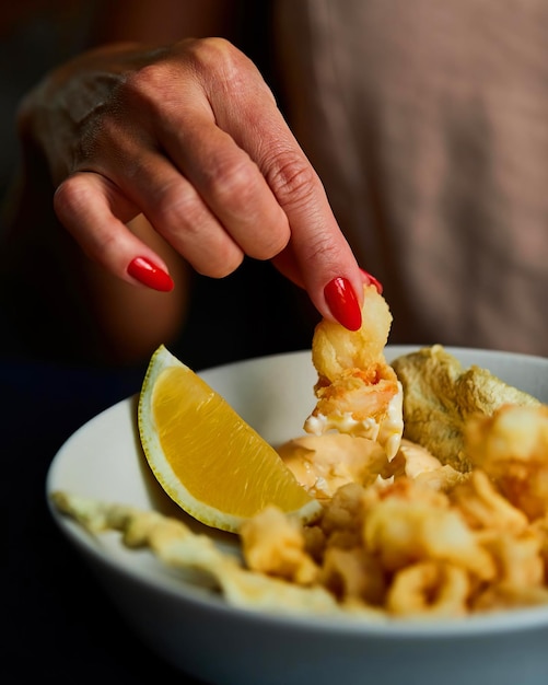 La main d'une femme aux ongles rouges mange un repas avec un quartier de citron.