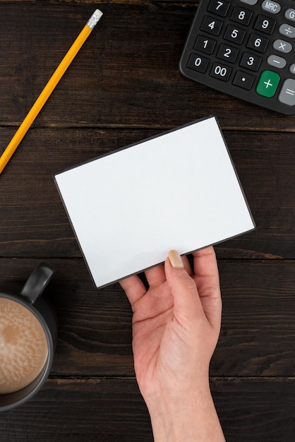 Main de femme ayant une feuille vierge avec copie espace tasse à café et papeterie sur fond de bois