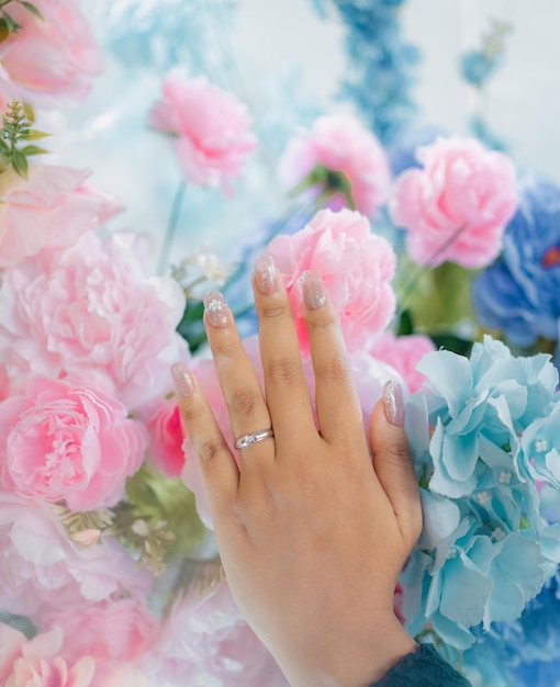 La main d'une femme avec une bague au doigt est entourée de fleurs.