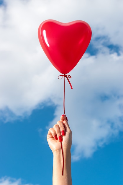 Main de femme avec ballon en forme de coeur sur fond de ciel.