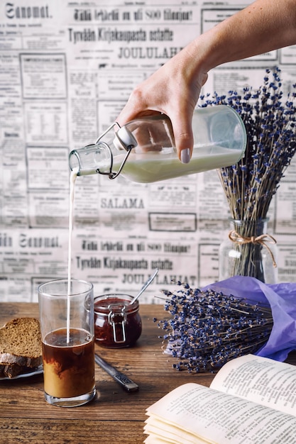 Main de femme avec une bouteille verser le lait en verre avec du café.