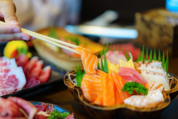 Une main de femme brandit des baguettes pour placer délicatement un sashimi de saumon frais sur une assiette