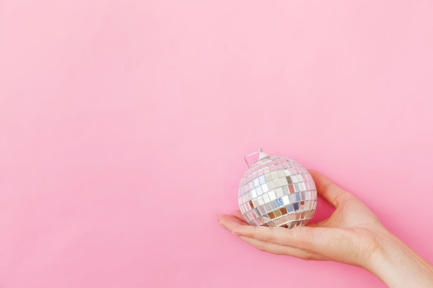 Main de femme de conception simplement minimale tenant la boule disco d'ornement de Noël isolée sur la pâte rose...