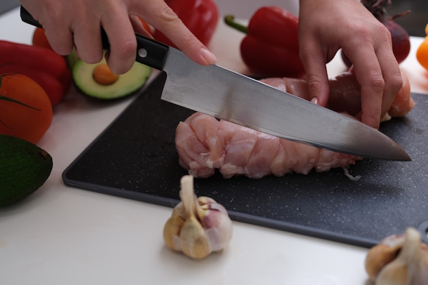 La main de femme coupe le filet de viande avec le couteau à bord à côté de l'ail