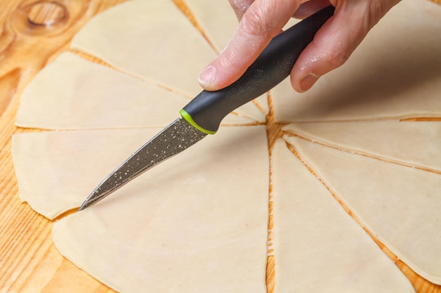 Une main de femme coupe la pâte avec un couteau de cuisine