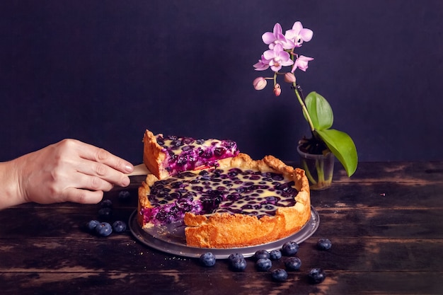 La main de la femme coupe et prend un morceau de tarte sablée rustique aux myrtilles