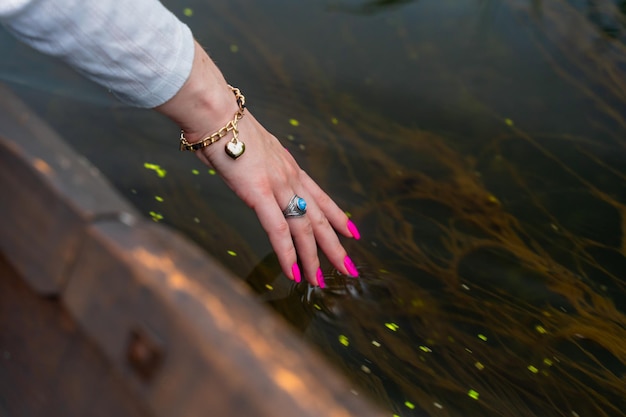 La main d'une femme dans un bracelet et une bague avec une manucure rose touche le gros plan de l'eau