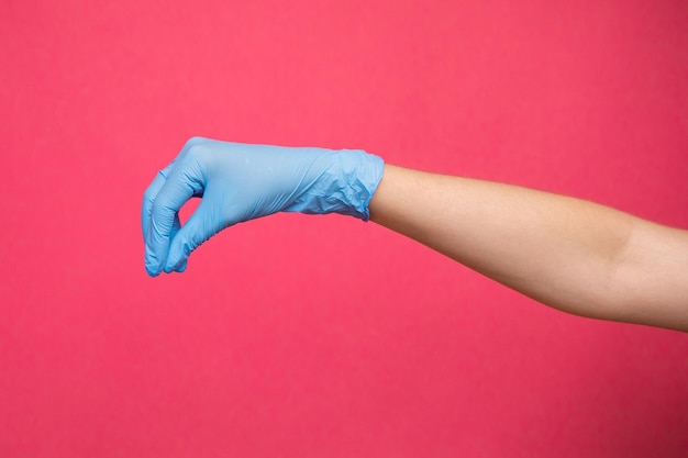 Main de femme dans un gant médical bleu faisant semblant de tenir un médicament sur fond rose