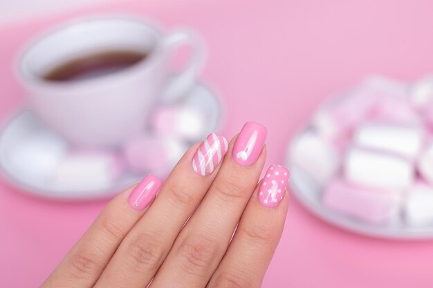 La main d'une femme avec du vernis à ongles rose à pois blancs et roses sur ses ongles