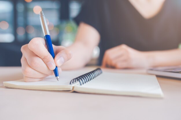 Une main de femme écrit sur un cahier avec un stylo.