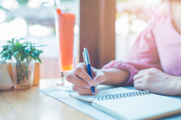 Une main de femme écrit sur un cahier avec un stylo.