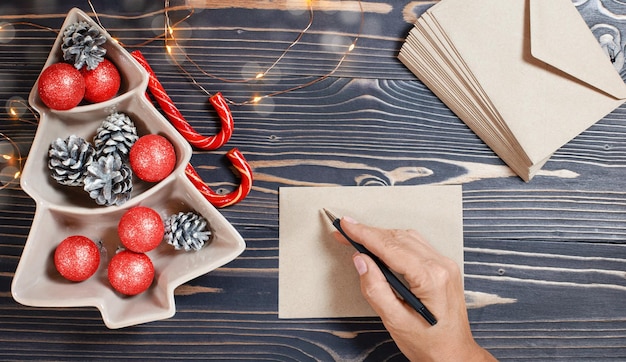 La main d'une femme écrit des voeux de Noël sur une enveloppe posée sur une table en bois