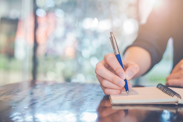 Main de femme écrivant sur un bloc-notes avec un stylo au bureau.