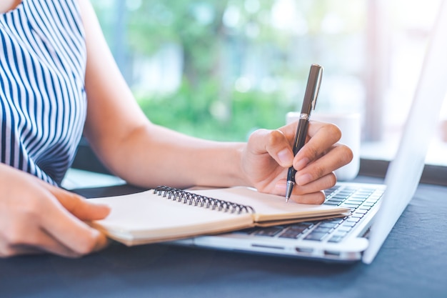 Main de femme écrivant sur le bloc-notes avec un stylo dans le bureau