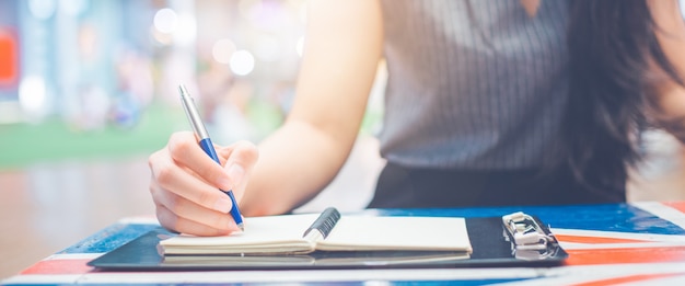 Main de femme écrivant sur un bloc-notes avec un stylo.