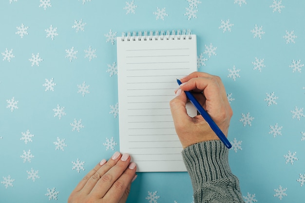 Main de femme écrivant dans un cahier vide orné de décorations de Noël