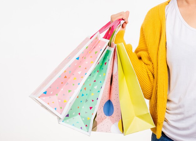 Main de femme, elle porte une chemise jaune tenant des sacs multicolores