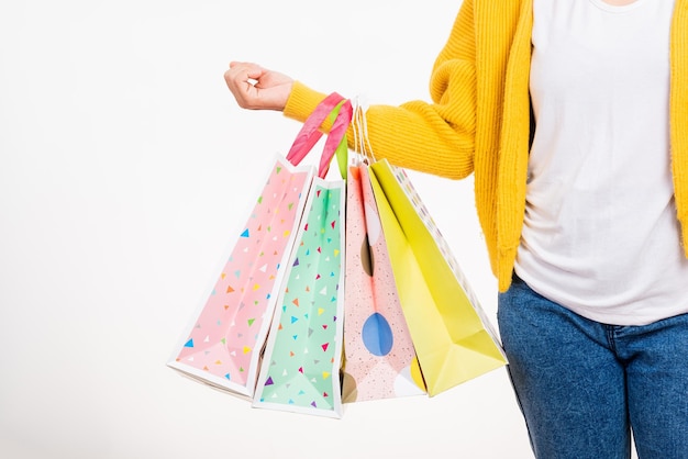 Main de femme, elle porte une chemise jaune tenant des sacs multicolores