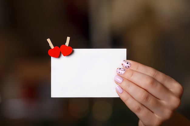 Main de femme est titulaire d'une carte en papier avec deux broches de coeur. Concept de Saint Valentin. Copyspace pour le texte.