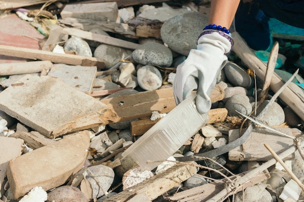 Main d'une femme avec une feuille de plastique et autour d'elle plus de déchets sur les pierres d'une plage. Copier l'espace